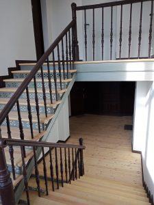 Widok na klatkę schodową, jasne drewniane schody, ciemne poręcze