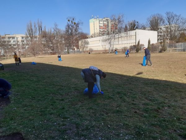 Widoczni na zdjęciu ludzie sprzątają rozległy teren zielony