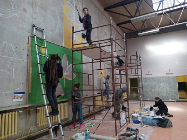 Artyści, stojący na rusztowaniach lub na podłodze, malujący mural