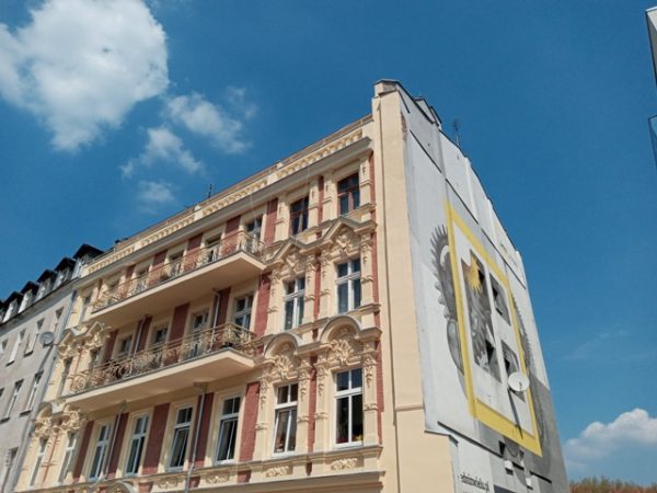Widoczny budynek narożny z wyremontowaną ścianą frontową oraz szczytową; na tej ostatniej mural