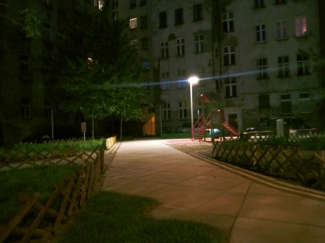 Zdjęcie wykonano nocą, widoczna alejka oraz lampa miejska oświetlająca po prawej stronie plac zabaw