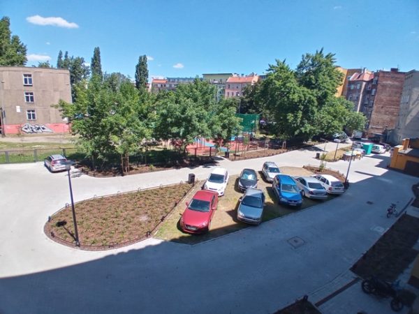 Zdjęcie z góry obrazujące plac podwórkowy z miejscami do parkowania oraz wyspami zieleni