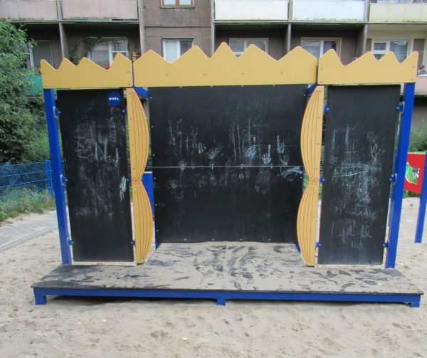 Urządzenie zabawowe na piaskowym placu zabaw. Widoczna jest scena z materiału, po którym można pisać kredą