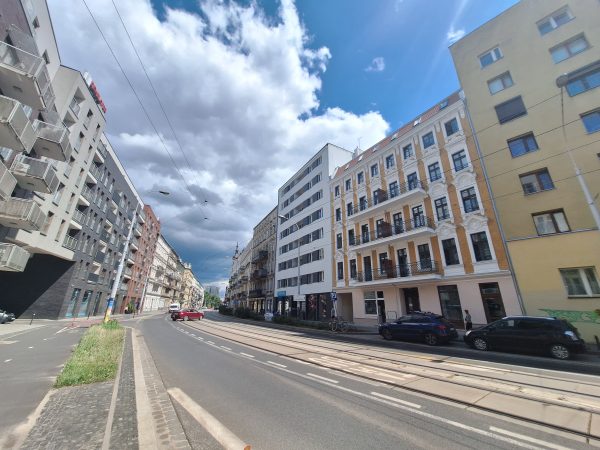 Widok na ulicę (pustą, bez aut); po bokach jezdni budynki w różnym stylu