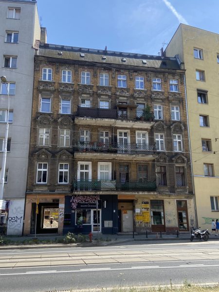 Zniszczona fasada kamienicy z XIX wieku, cztery kondygnacje, szara