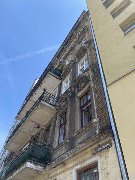 Widok od dołu na zniszczoną fasadę, na pierwszym planie stolarka okienna