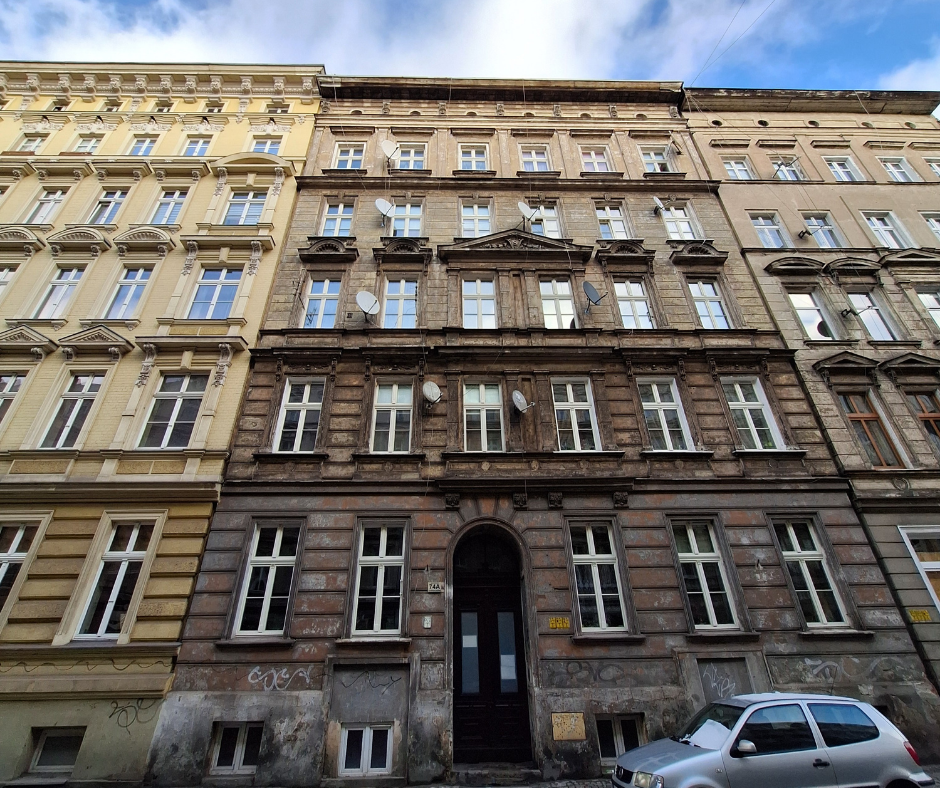 Widok na fasadę miejskiej kamienicy z XIX wieku. Widok od dołu; budynek sąsiaduje z innymi kamienicami